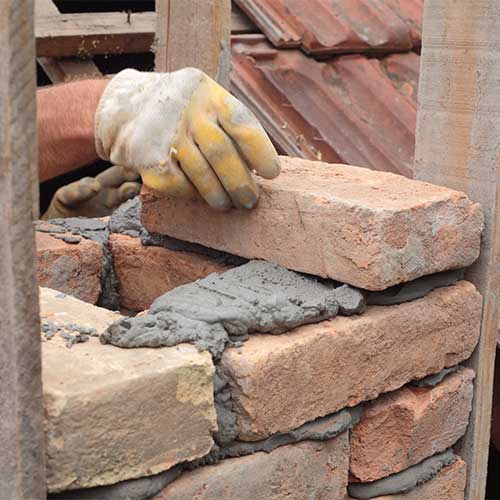 Stock photo of gloved hand laying brick for a chimney.  Mortar between bricks.