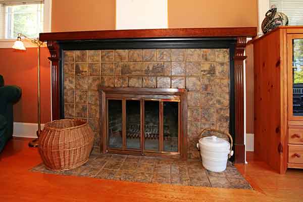 Stock photo of newly installed fireplace door.  Tiled hearth and surround wooden mantel.  Basket and bucket sitting on the hearth.  To the right is a wardrobe.