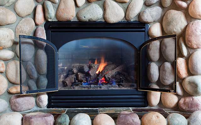 Stock photo of beautiful large stone fireplace surround with gas insert, tile hearth and double screen doors.