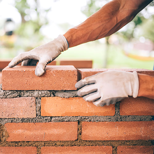 Stock photo of hands with gloves stacking mortar and bricks otherwise known as tuckpointing.
