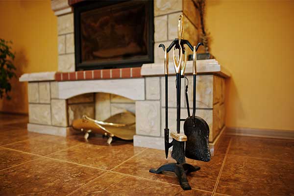 Stock photo of fireplace accessories in front of a beautiful unique fireplace.  Hearth stand about a foot tall with a place in the middle for wood.  The insert stands on top and is surrounded with the same stone as the base.