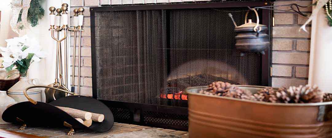 Stock photo of fireplace accessories.  Pot on swinging level, bucket with pine cones and scuttle with small logs.  The fireplace is screened and their are flowers to the left of the fireplace.