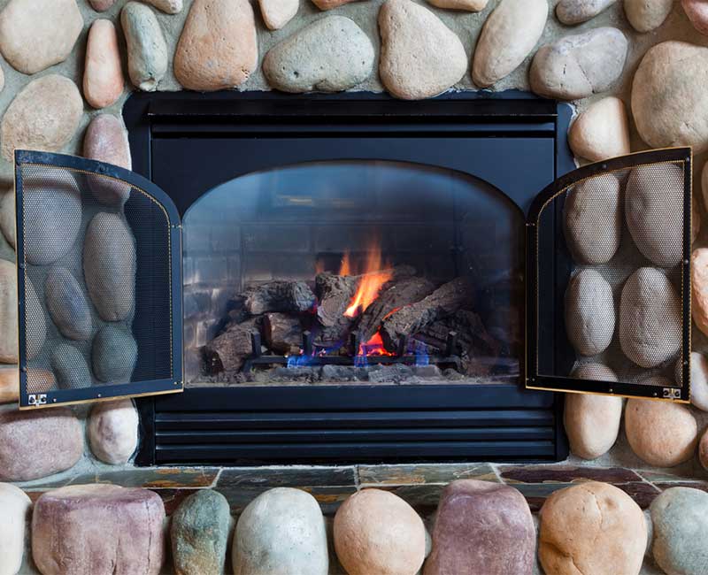 Stock photo of beautiful large stone fireplace surround with gas insert, tile hearth and double screen doors.